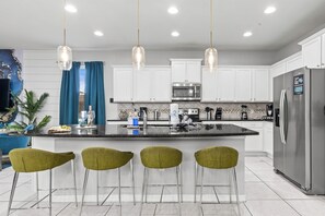 A modern kitchen with white cabinets, stainless steel appliances, and a central island with bar stools. - Sleeps 21 / Disney & Universal Retreat w/ Game Room + Pool, Spa (Kissimmee)