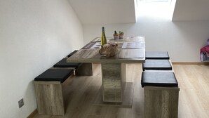 A room with a sloped ceiling, a skylight, a wooden dining table with black cushions, and a potted plant. - At Léa's cozy little nest (Muhlbach)