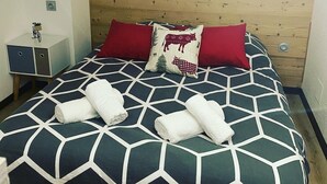 A bed with a geometric patterned bedspread, two red pillows, and two rolled towels. - At Léa's cozy little nest (Muhlbach)