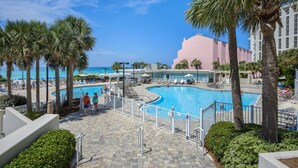 A pool area with palm trees, a clear sky, and a view of the ocean. - Stunning Gulf views, 2BR Corner Unit, at Tops'l resort! (Miramar Beach)