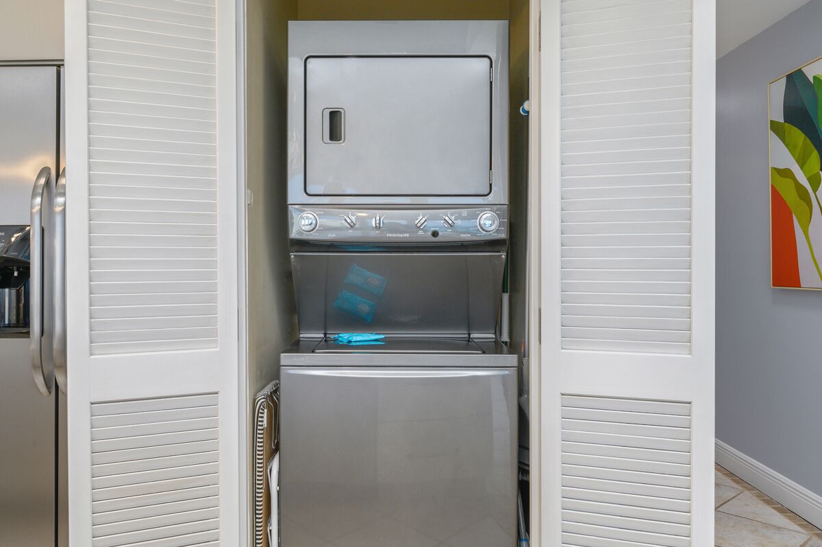 A compact kitchen with a built-in microwave and refrigerator, a small window, and a colorful abstract painting on the wall.