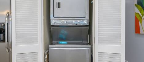 A compact kitchen with a built-in microwave and refrigerator, a small window, and a colorful abstract painting on the wall.