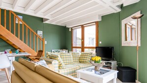 En stue med grøn væg, en trætrap, en beige sofa, et hvidt sofabord og et fjernsyn.