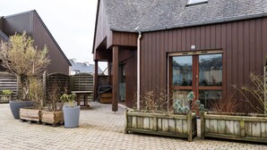 En bygning med mørkebrun facade, skråt tag og et stort vindue. Der er træplantekasser med forskellige planter foran bygningen.
