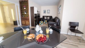 Un coin repas avec une table en verre mise pour le petit-déjeuner, comprenant des croissants, des fruits et des boissons.