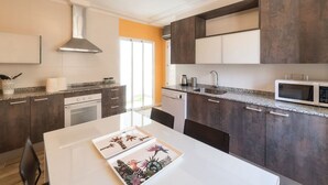 Une cuisine moderne avec des meubles de couleur sombre, un plan de travail blanc et une hotte en acier inoxydable.