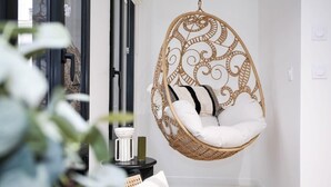 A wicker hanging chair with white cushions in a room with white walls and a black floor.