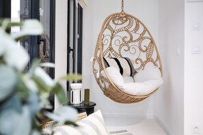 A wicker hanging chair with white cushions in a room with white walls and a black floor.
