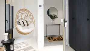 A room with a hanging chair, a console table with a vase, a dark door, and a hallway leading to another room.