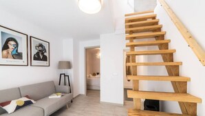 Una sala de estar moderna con una escalera de madera, un sofá gris y obras de arte enmarcadas en la pared.