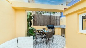 Un espacio exterior acogedor con sofá, mesa de comedor, sillas, una parrilla y una pequeña cocina.