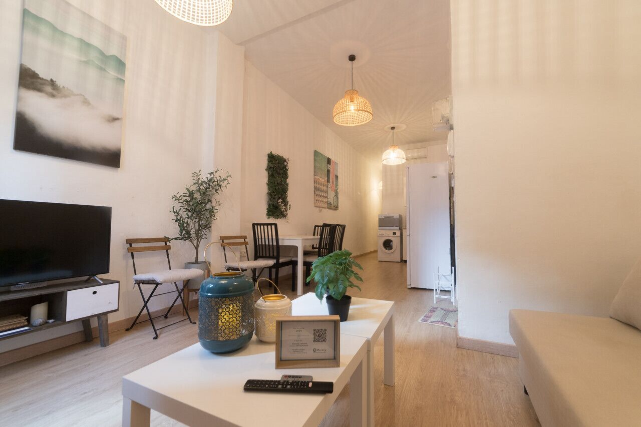 En moderne stue med et fladskærms-tv, et spiseområde med stole og et bord, og et køkken med en vaskemaskine.