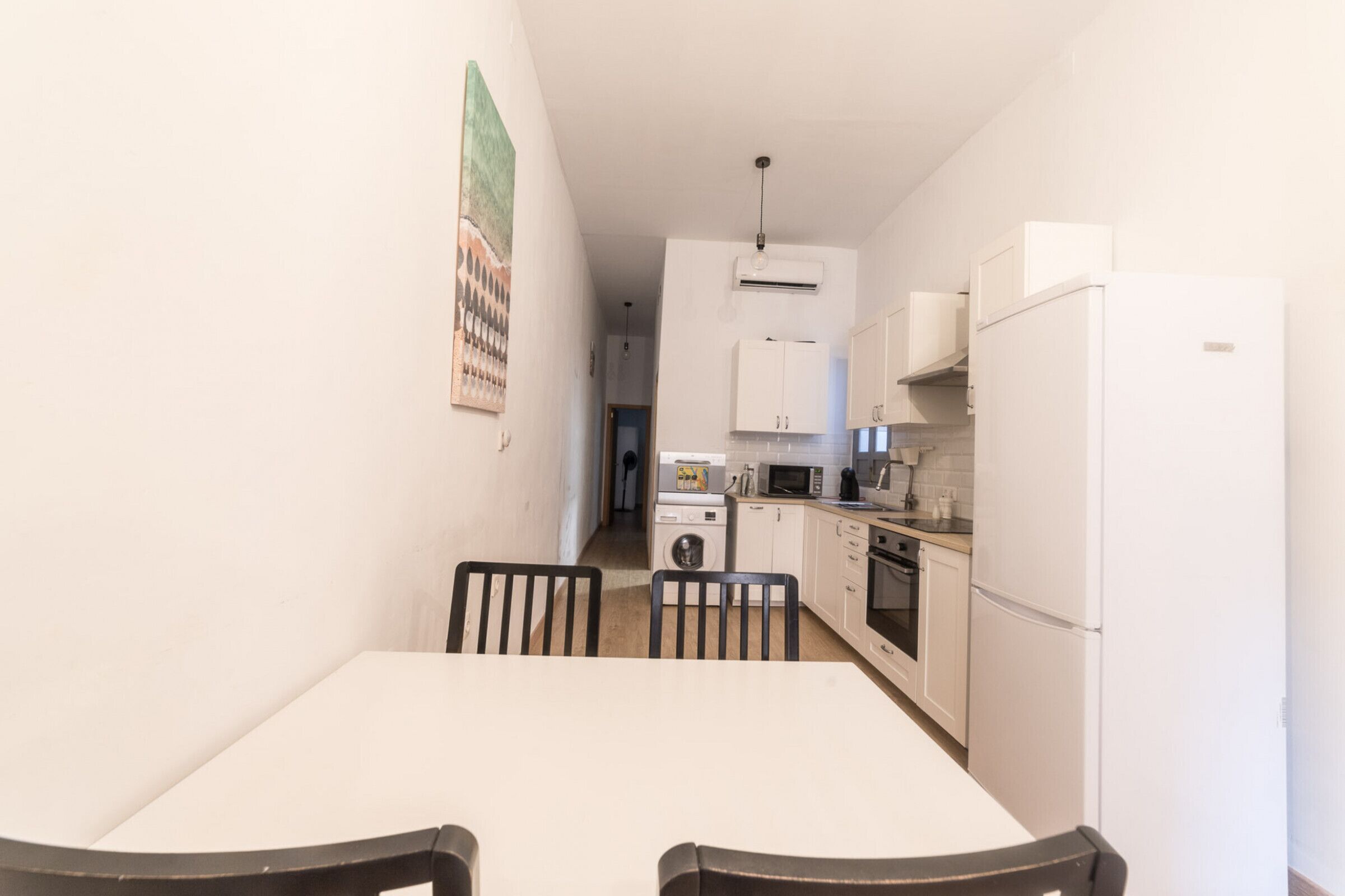 A compact kitchen with white cabinets, a microwave, a refrigerator, and a dining table with chairs.