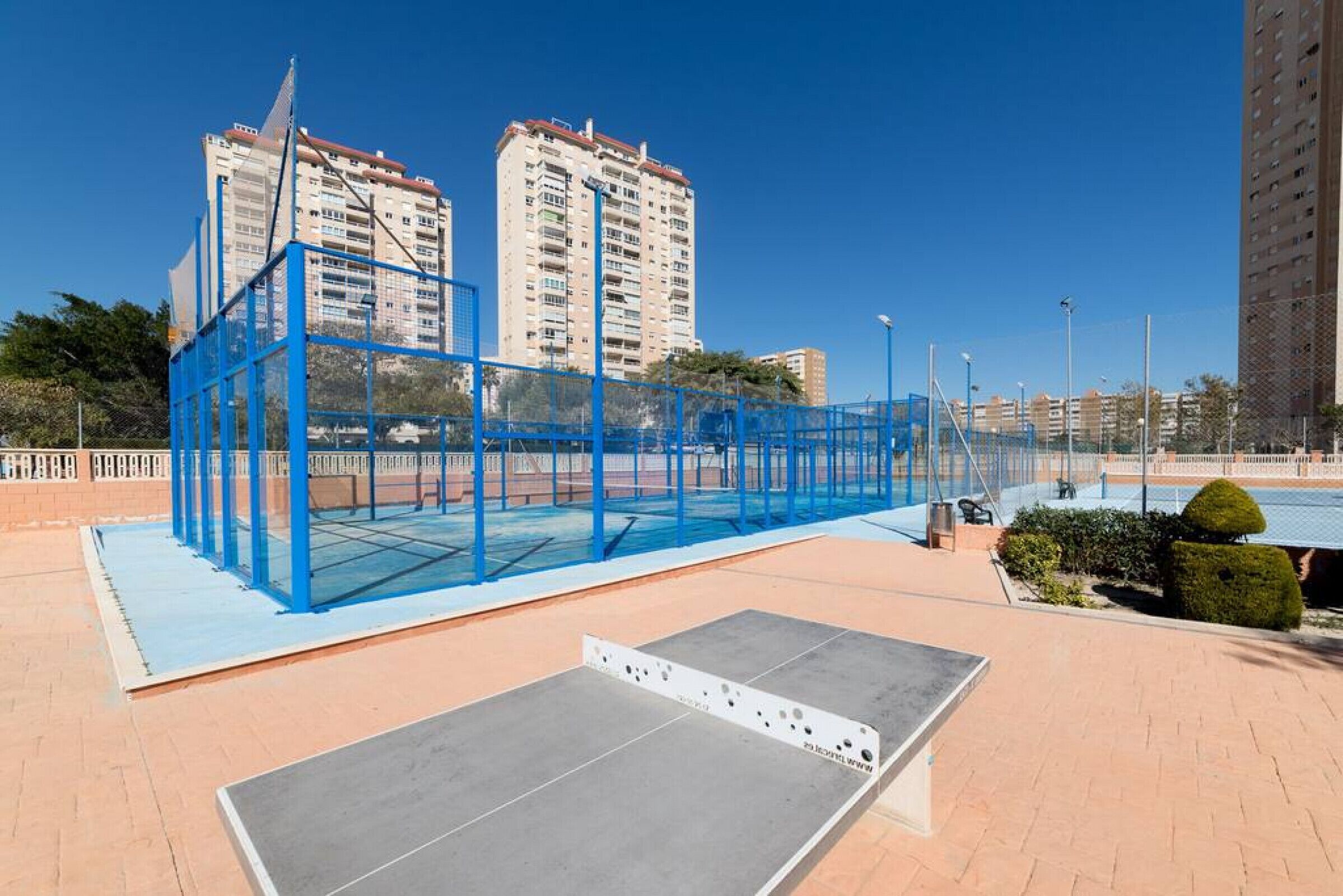 Un complexe sportif en plein air doté d’une structure métallique bleue, d’une plateforme en béton et entouré de bâtiments.