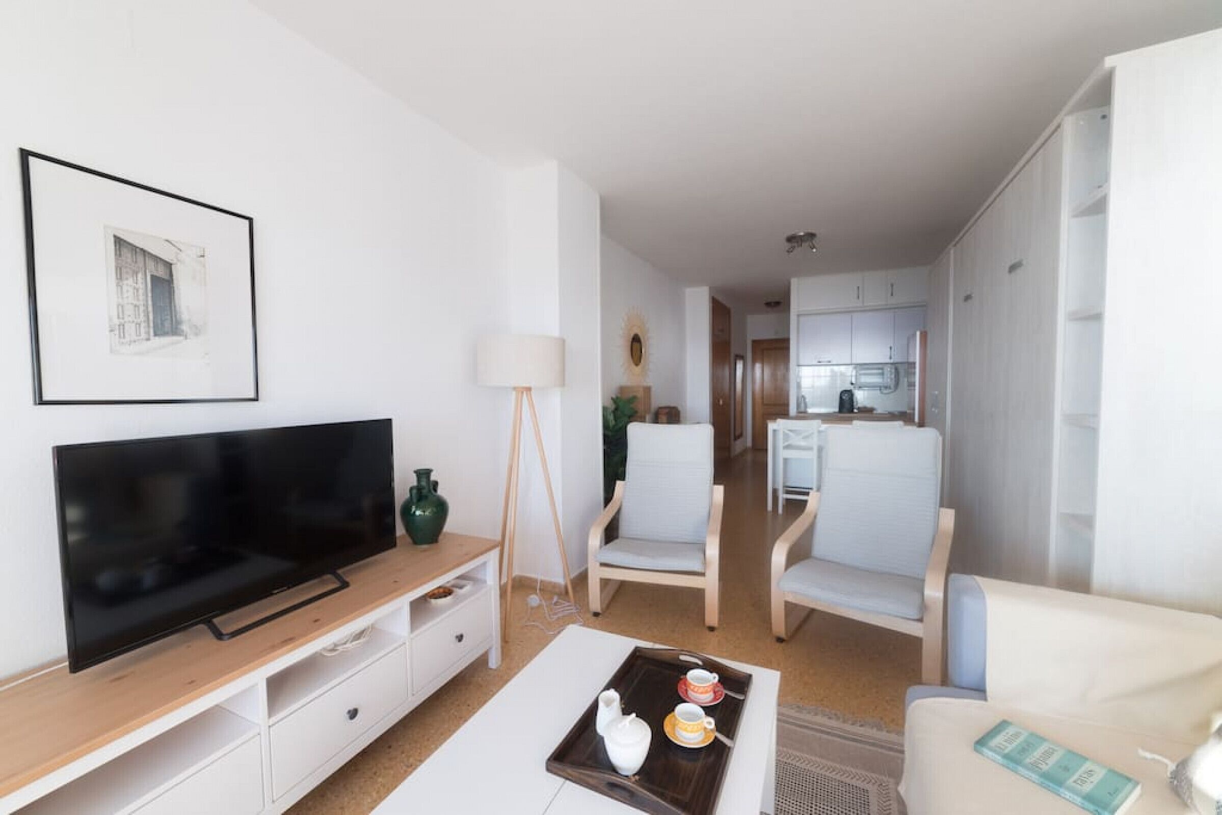 A modern living room with a flat-screen TV, a coffee table with a tray, and a sofa.
