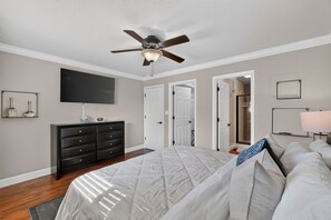 A bedroom with a bed, a dresser, a ceiling fan, a television, and a door leading to another room. - Oasis Pool, Outdoor Kitchen and Grill, Arcade Room, Movie Room, Sleep up to 13 (Fresno)