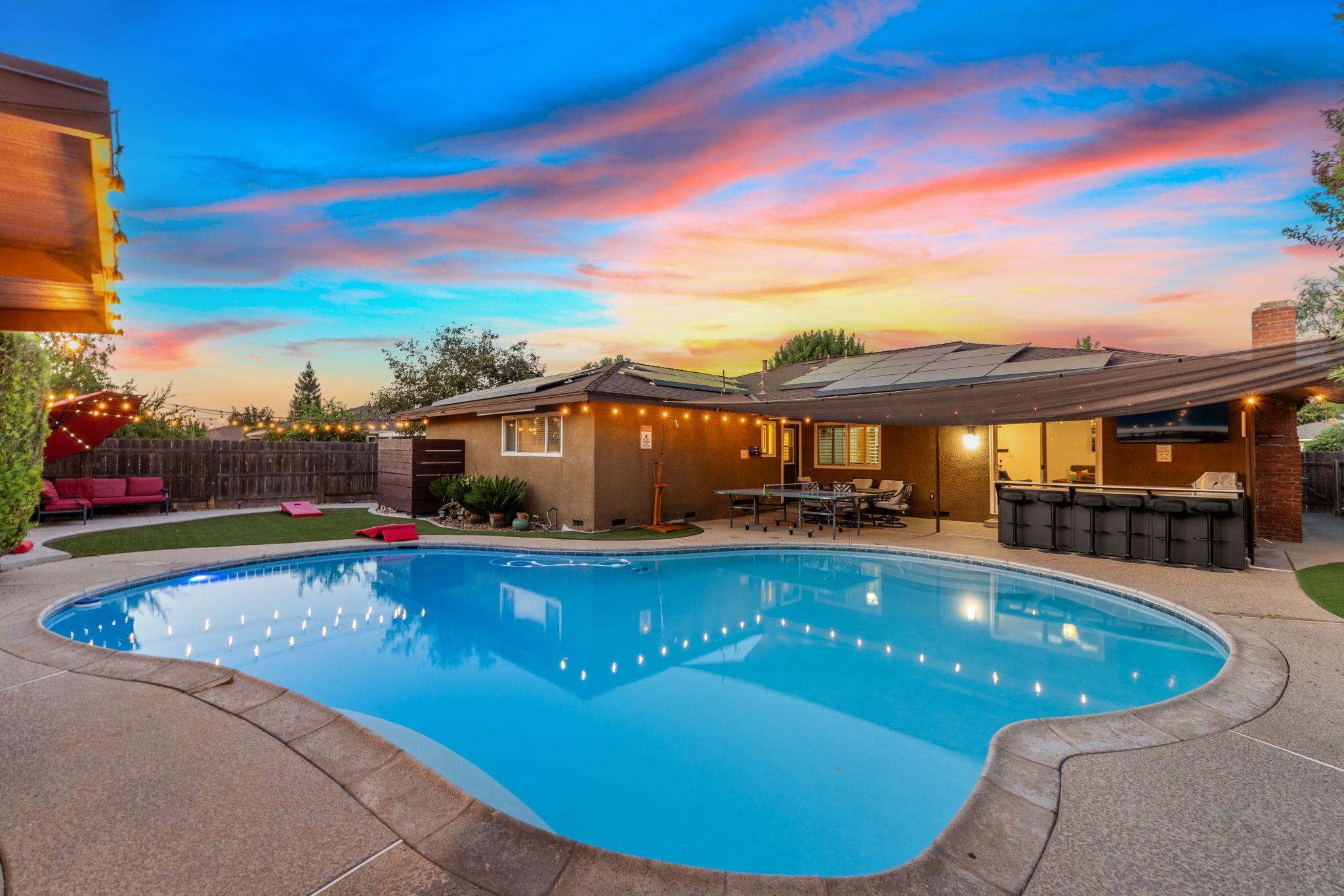 A backyard with a swimming pool, a barbecue area, and a covered patio.