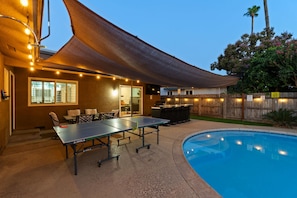 Un espace extérieur avec une piscine, une table de ping-pong, un barbecue et un coin salon abrité.
