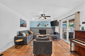 A living room with a fireplace, a sofa set, a coffee table, a television, and a piano. - Oasis Pool, Outdoor Kitchen and Grill, Arcade Room, Movie Room, Sleep up to 13 (Fresno)