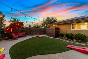 Un jardin avec une pelouse artificielle, un parasol rouge et des guirlandes lumineuses.