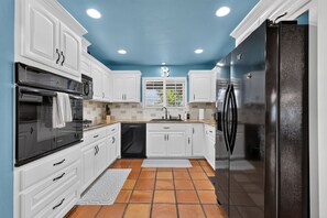 A kitchen with white cabinets, a black refrigerator, and a window with a letter 'B' above it. - Oasis Pool, Outdoor Kitchen and Grill, Arcade Room, Movie Room, Sleep up to 13 (Fresno)