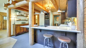 A rustic kitchen with wooden beams, a white countertop, and two stools. - Luxe Cabin in the Woods: Walk to Lake! (Gaston)