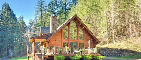 A log cabin with a stone chimney, a balcony, and potted plants.
