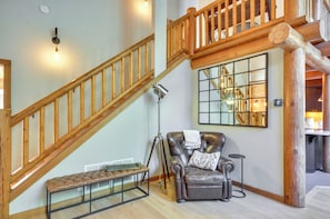 Una escalera con barandillas de madera, un sillón de cuero con un cojín decorativo, un banco y un espejo grande en la pared.