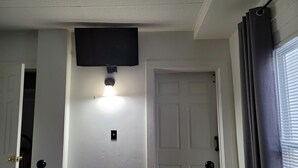 Ett sovrum med en säng, en väggmonterad TV, en lampa och två dörrar.