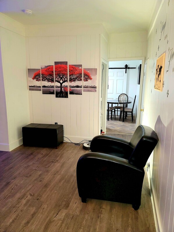 Un salon avec un canapé en cuir noir, un coin repas avec une table et des chaises, et un mur orné de trois tableaux représentant un arbre rouge.