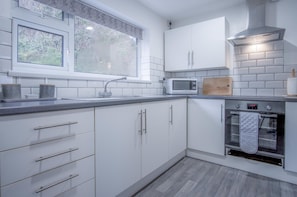 A modern kitchen with white cabinets, a stainless steel range hood, a microwave, and an oven.