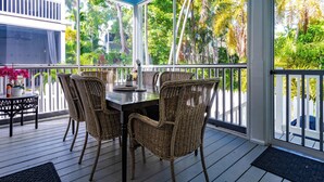 Une terrasse extérieure couverte, dotée d’une table à manger et de chaises en osier, et entourée de grandes fenêtres offrant une vue sur la végétation tropicale.