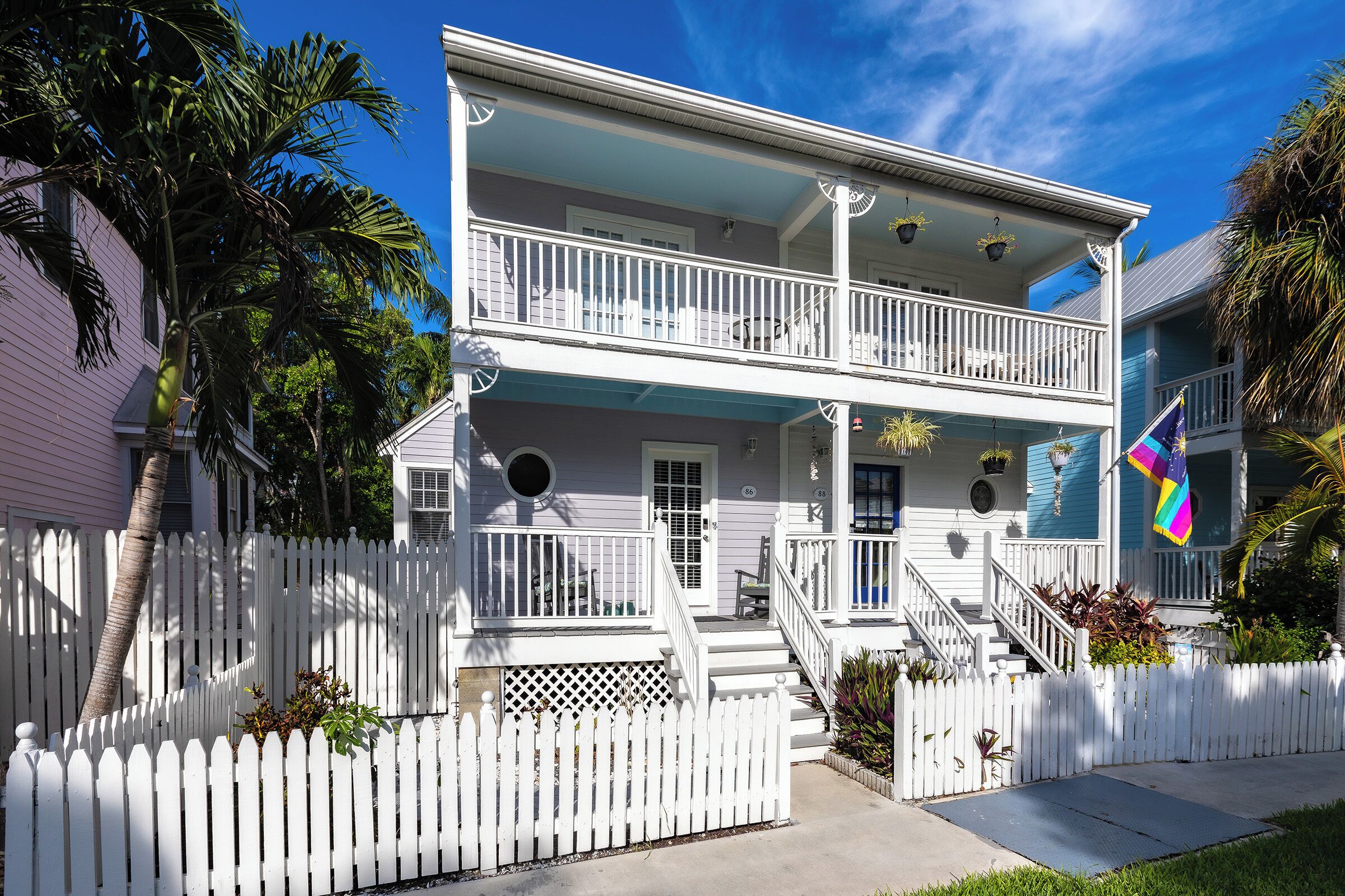 A two-story house with a white picket fence, a balcony, and a flag.