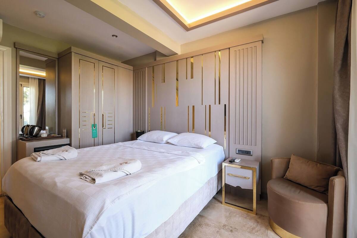 Quarto de hotel com uma cama grande, mesas de cabeceira, uma cadeira e um guarda-roupa.