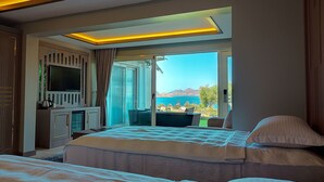 A modern hotel room with a large bed, a TV, a desk, and a view of the sea. - Roas Hotel (Bodrum)