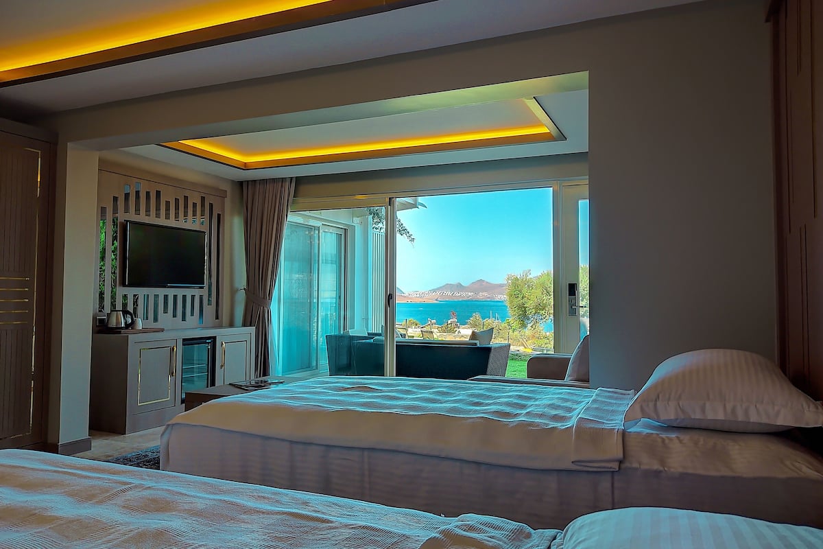 Quarto de hotel moderno com uma cama grande, televisão, escrivaninha e vista para o mar.
