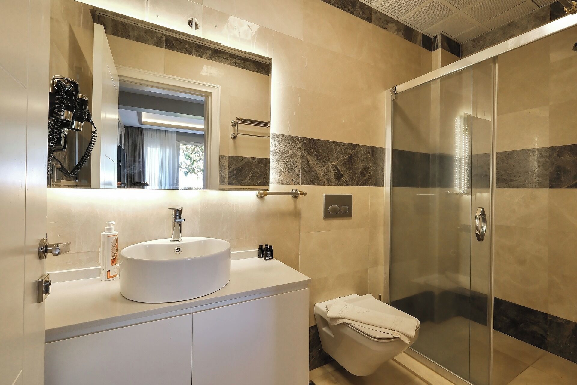 Un baño moderno con un espejo grande, un lavabo y una ducha con mampara de vidrio.
