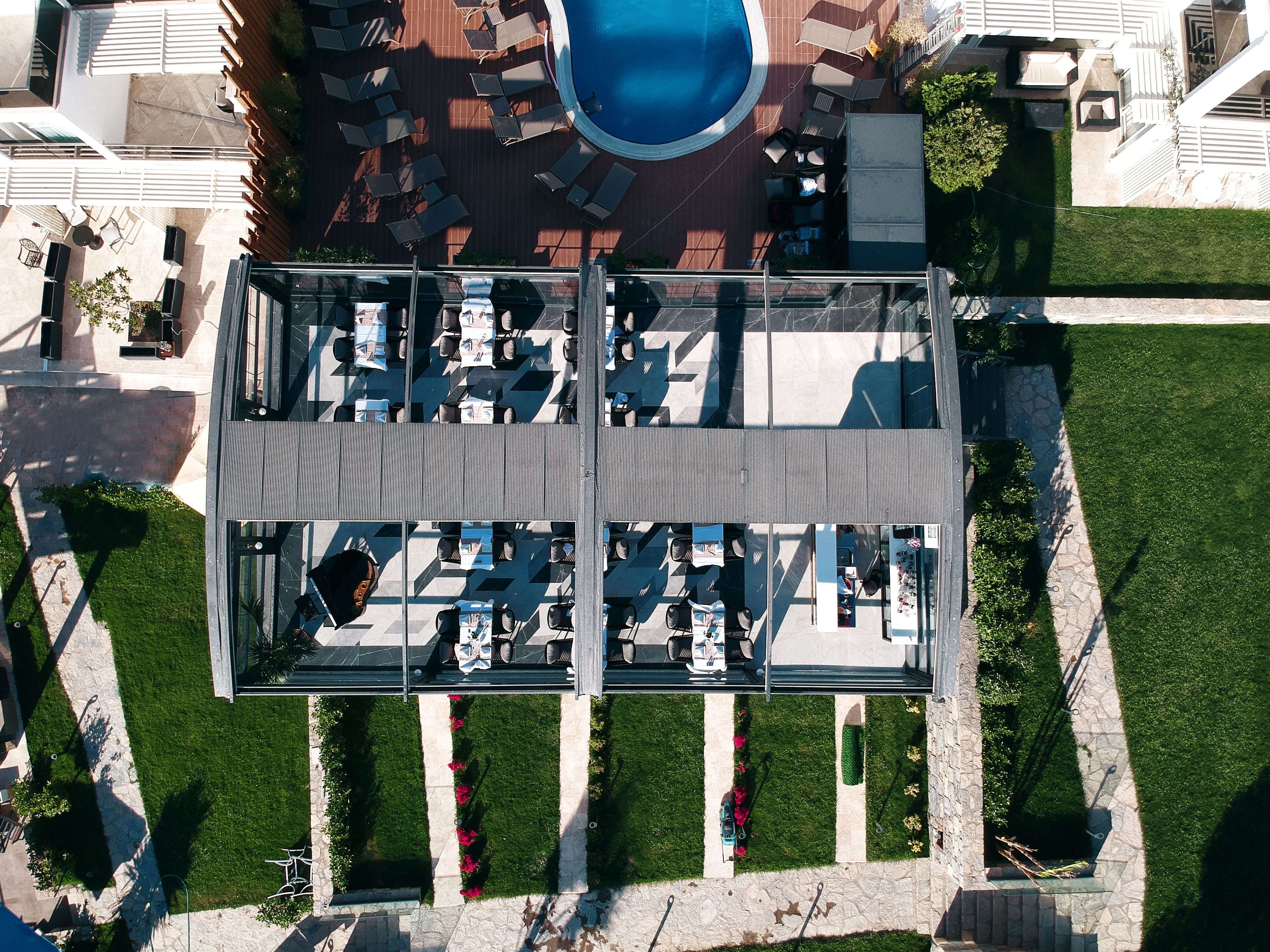 An aerial view of a modern hotel with a rooftop pool, outdoor seating area, and well-maintained gardens.