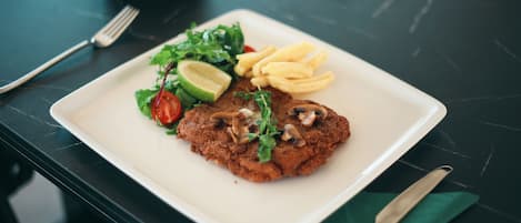 A plate with a meat patty, fries, and a salad on a dark table.