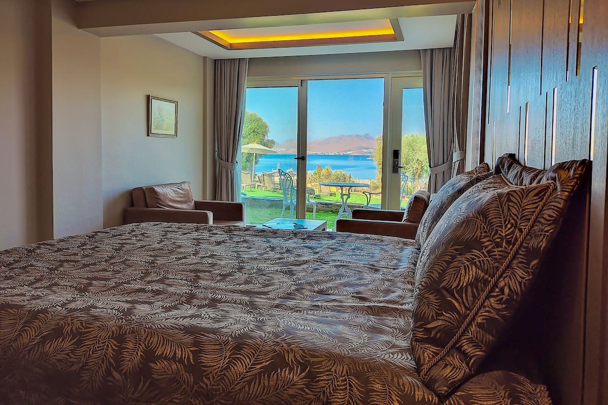 Quarto com cama grande, vista para o mar e área de refeições com mobiliário de exterior.