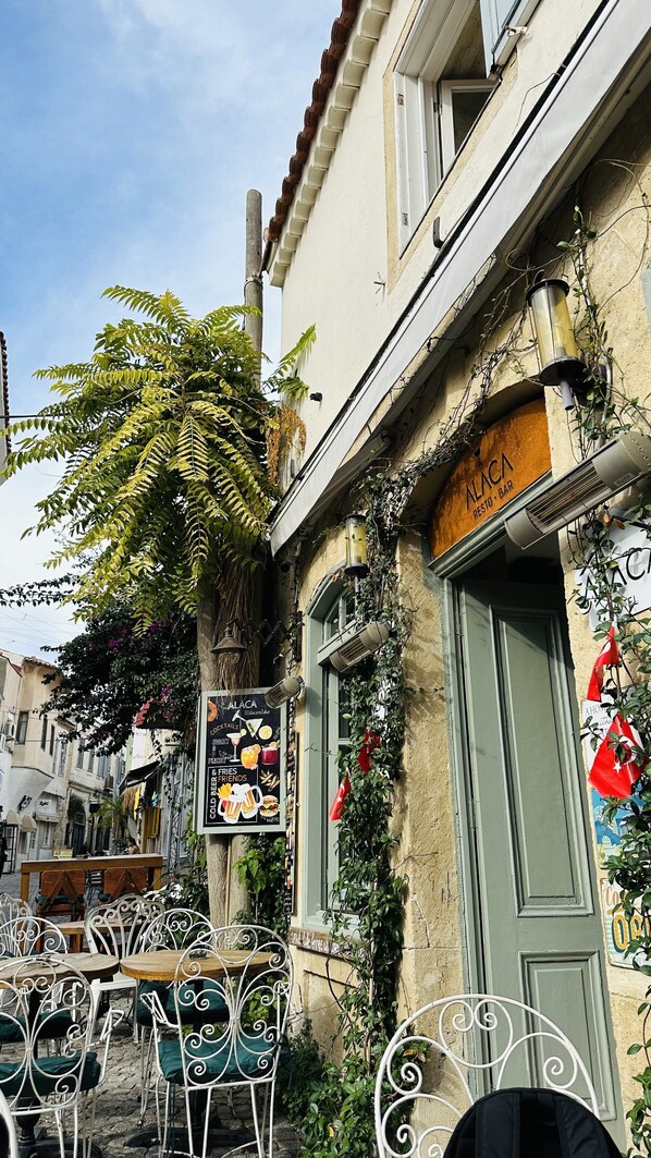 Un café avec une terrasse, un tableau affichant le menu et un bâtiment avec une porte verte.
