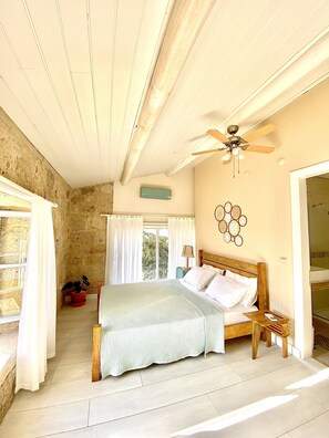 A bedroom with a wooden bed, a ceiling fan, a window with curtains, and a stone wall. - Alaca Butik Otel (Cesme)