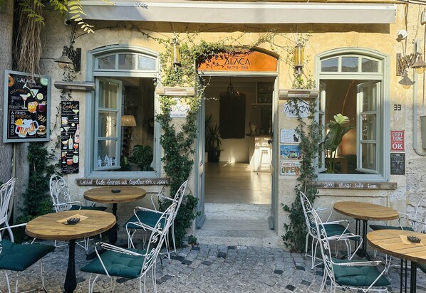 An outdoor café with tables and chairs, a sign reading "ALACA RESTO BAR", and a menu board on the wall. - Alaca Butik Otel (Cesme)