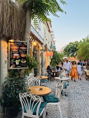 An outdoor cafe with tables and chairs, a menu board, and a building with a sign. - Alaca Butik Otel (Cesme)