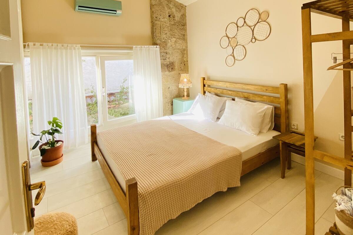 Un dormitorio con cama de madera, ventilador de techo, pared de piedra y vistas al exterior.