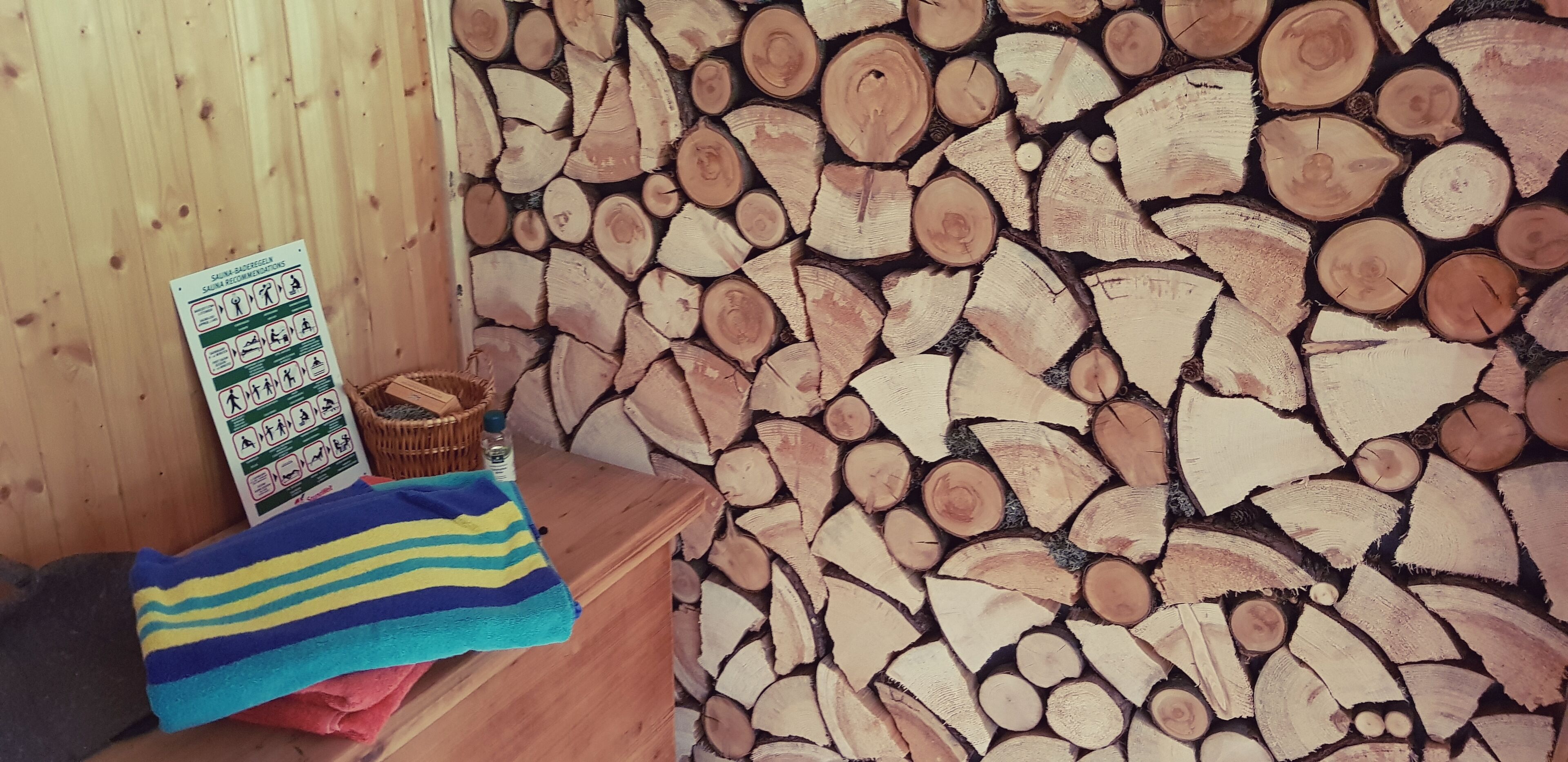 Sala de sauna com parede de madeira feita de toras empilhadas, uma toalha, um cesto e uma placa com instruções para a sauna.