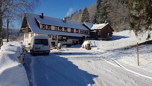En snötäckt byggnad med ett sluttande tak, ett trästaket och en snötäckt uppfart.