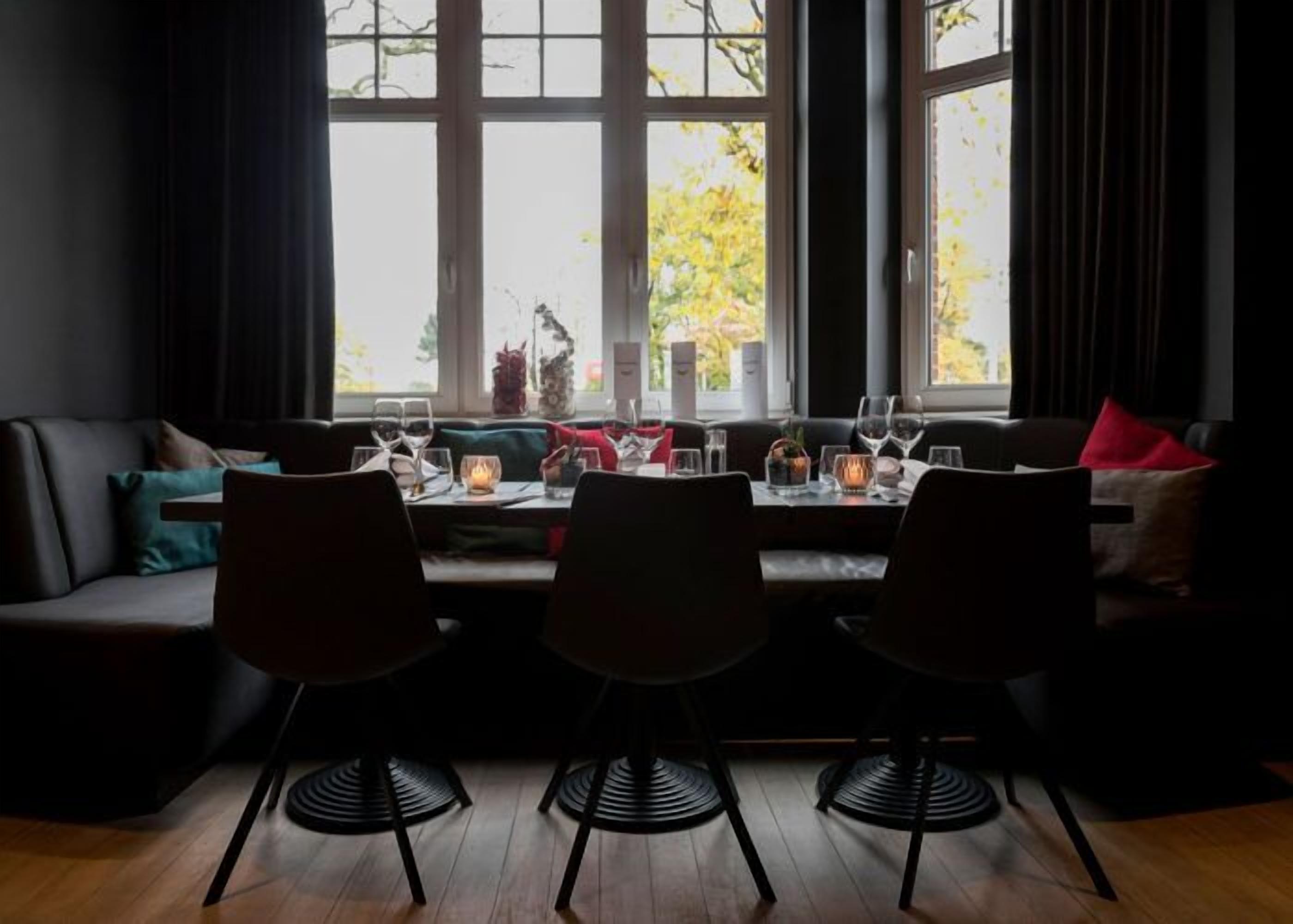 A dining area with a table set for three, a sofa, and large windows with a view of trees.