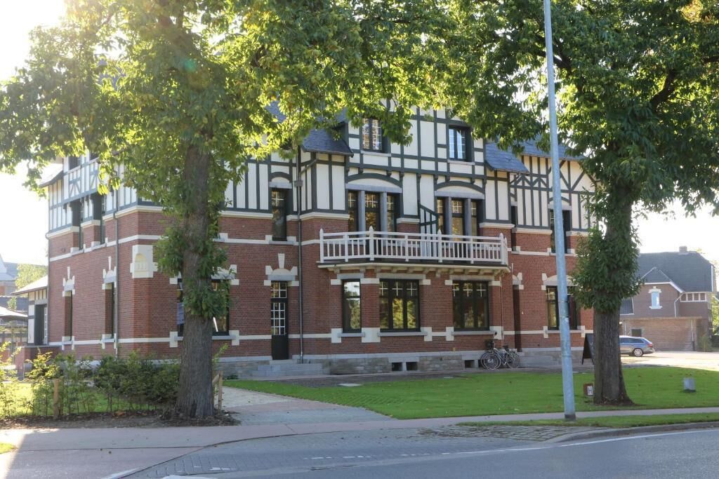 A two-story building with a balcony, brick walls, and a small garden area.