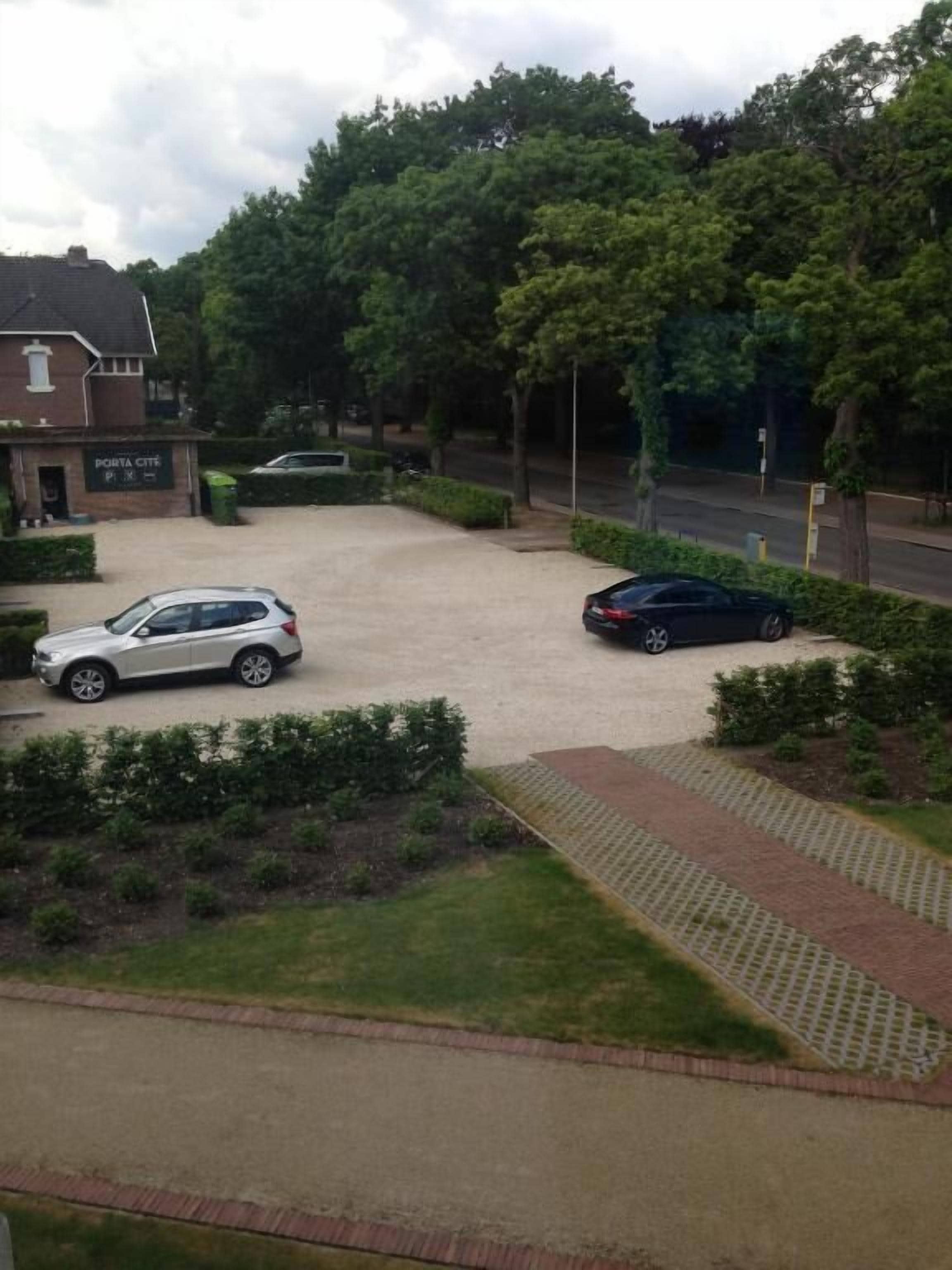 A parking area with two cars, a building labeled "PORTA CITTA," and surrounding greenery.